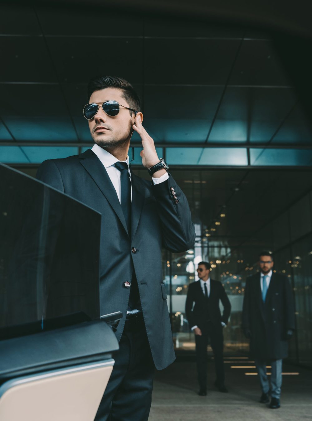 bodyguard opening car door for businessman and listening security earpiece